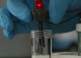 A gloved hand operates a red LED indicator in a laboratory setting, showcasing precise scientific experimentation.
